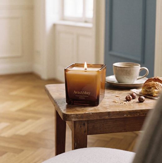 Candela Ava&May Viennese Coffee accesa su tavolino di legno con tazza di caffe, croissant e nocciole