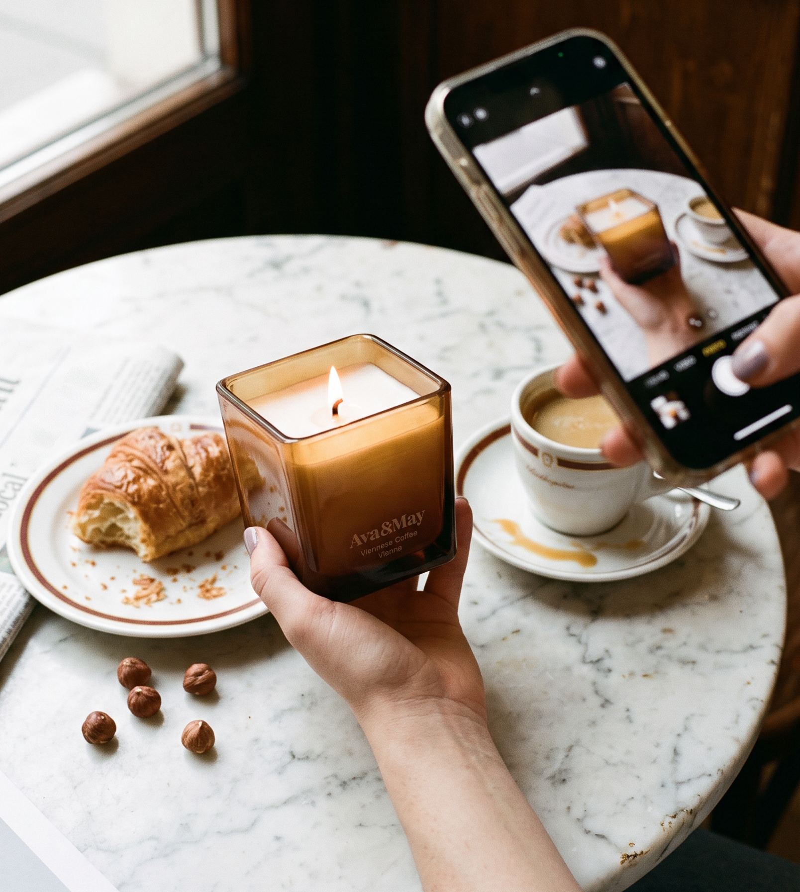 Candela Ava&May Viennese Coffee 220 grammi accesa con tazza di caffe, croissant e mano che la fotografa con un telefono